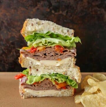 Stack of two halves of a roast beef sandwich next to potato chips.