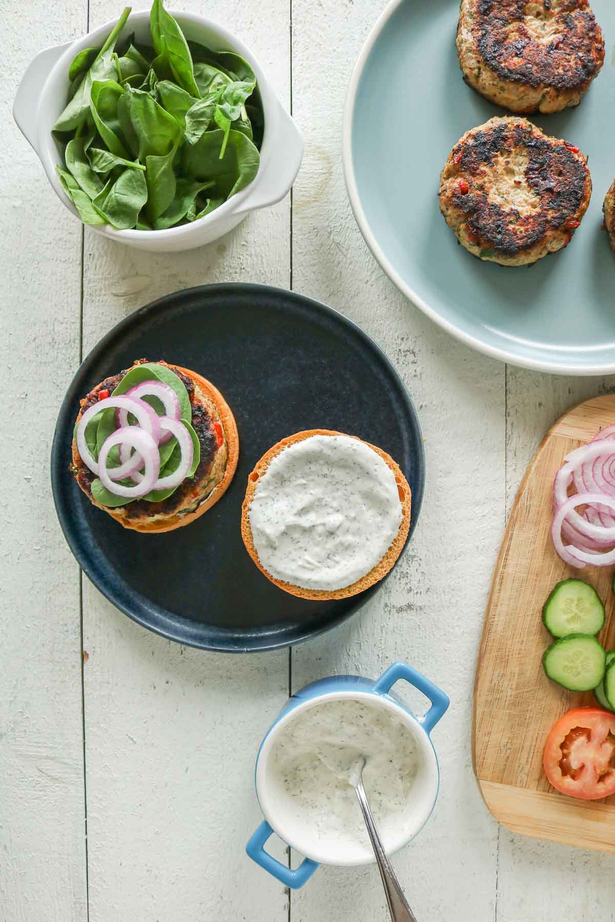 Assembling a Mediterranean ground chicken burger with toppings.