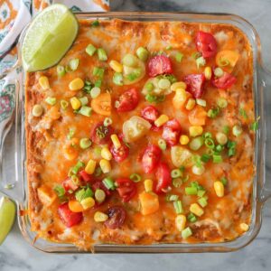 Cheesy refried bean dip in a baking dish with toppings.