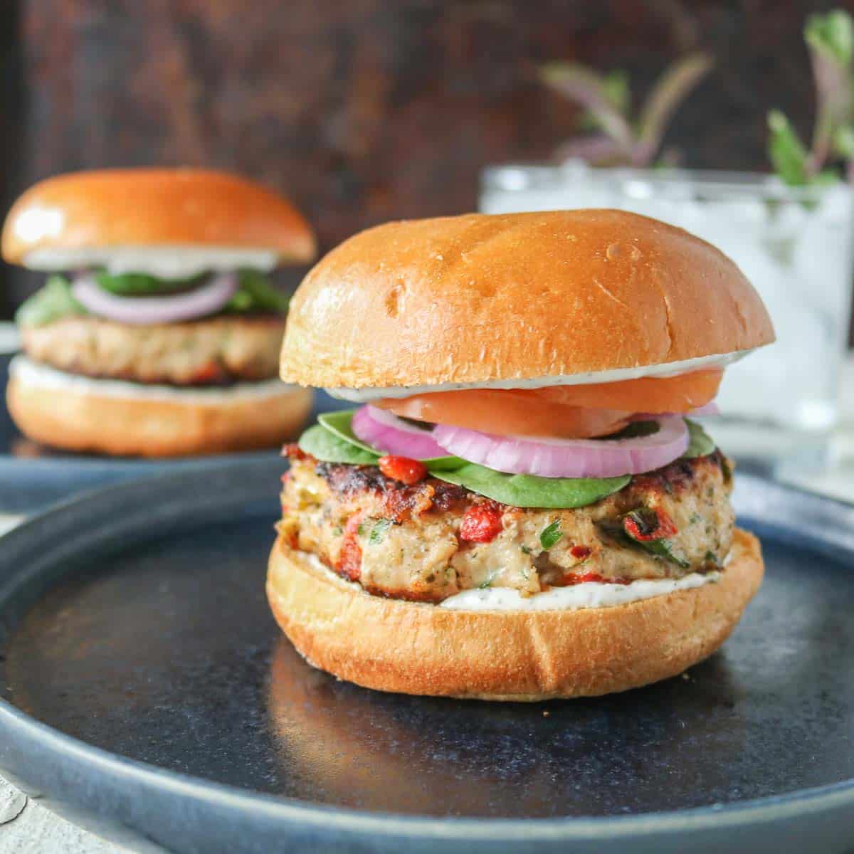 Two Mediterranean ground chicken burgers on plates with glasses of water.