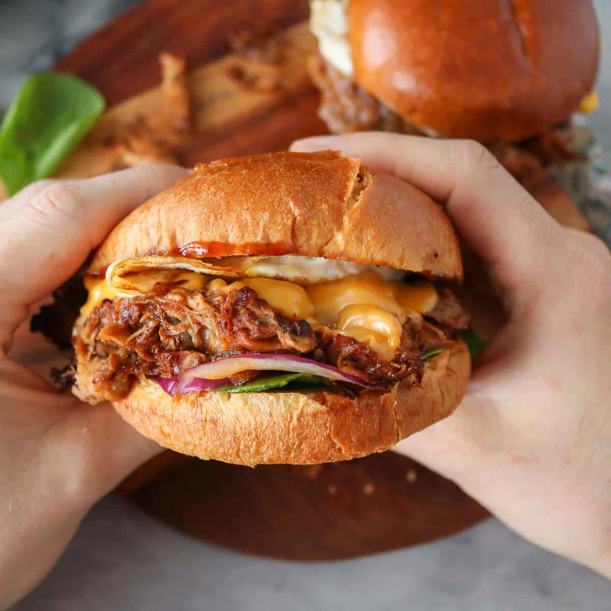 Two hands holding a pulled pork breakfast sandwich.