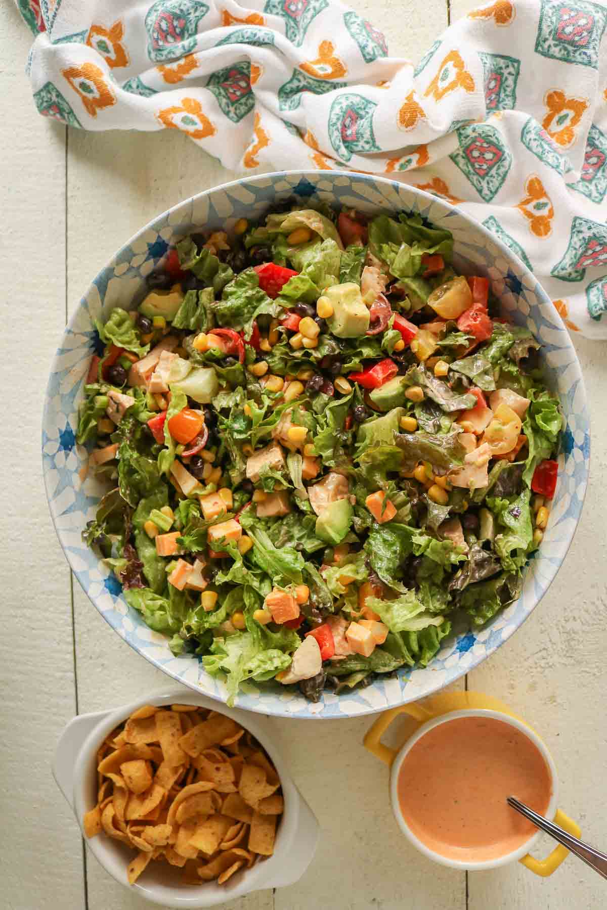 Southwest chicken salad in a serving bowl alongside corn chips and chipotle salad dressing.