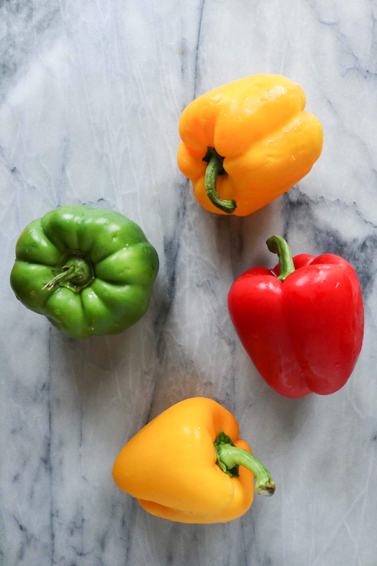 Four bell peppers on a marble board.