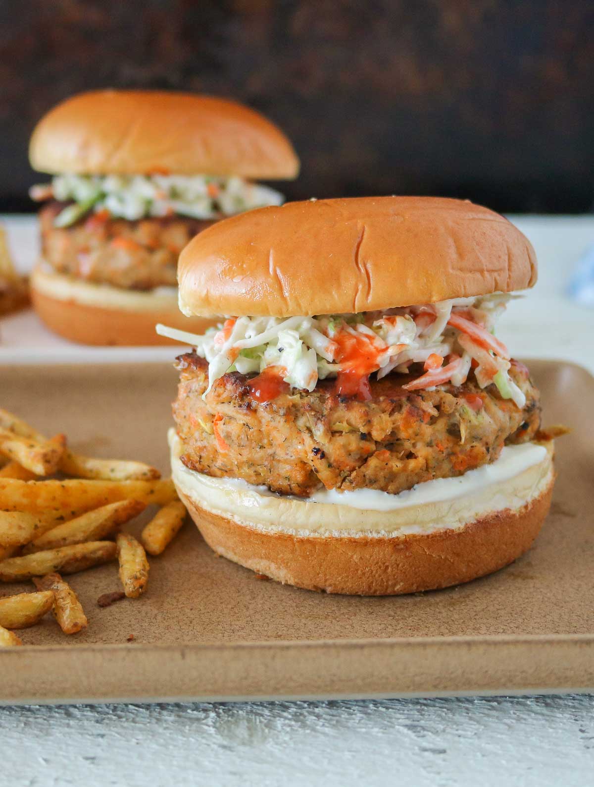 Two buffalo chicken burgers and fries, each on a plate, one plate in front of the other.