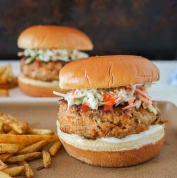 Two buffalo chicken burgers and fries, each on a plate, one plate in front of the other.