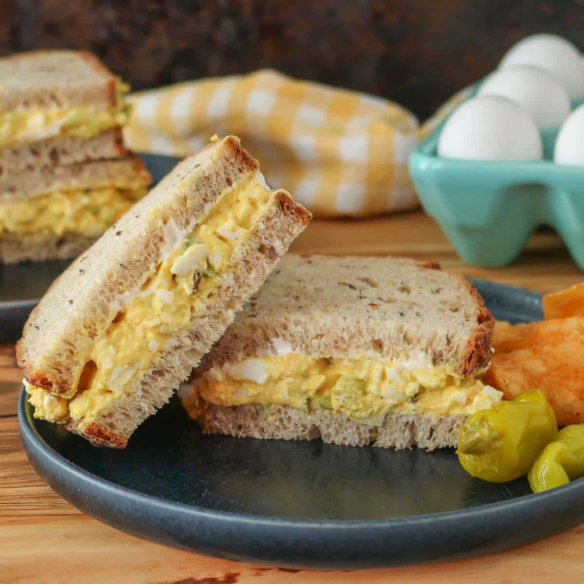 Two halves of a curried egg salad sandwich on a plate, one half resting on the other half.