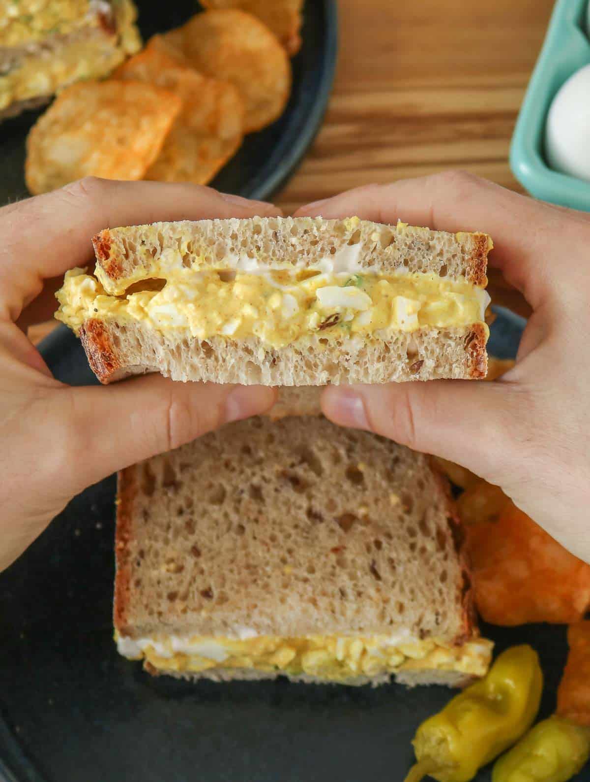 Two hands holding one half of an egg salad sandwich.