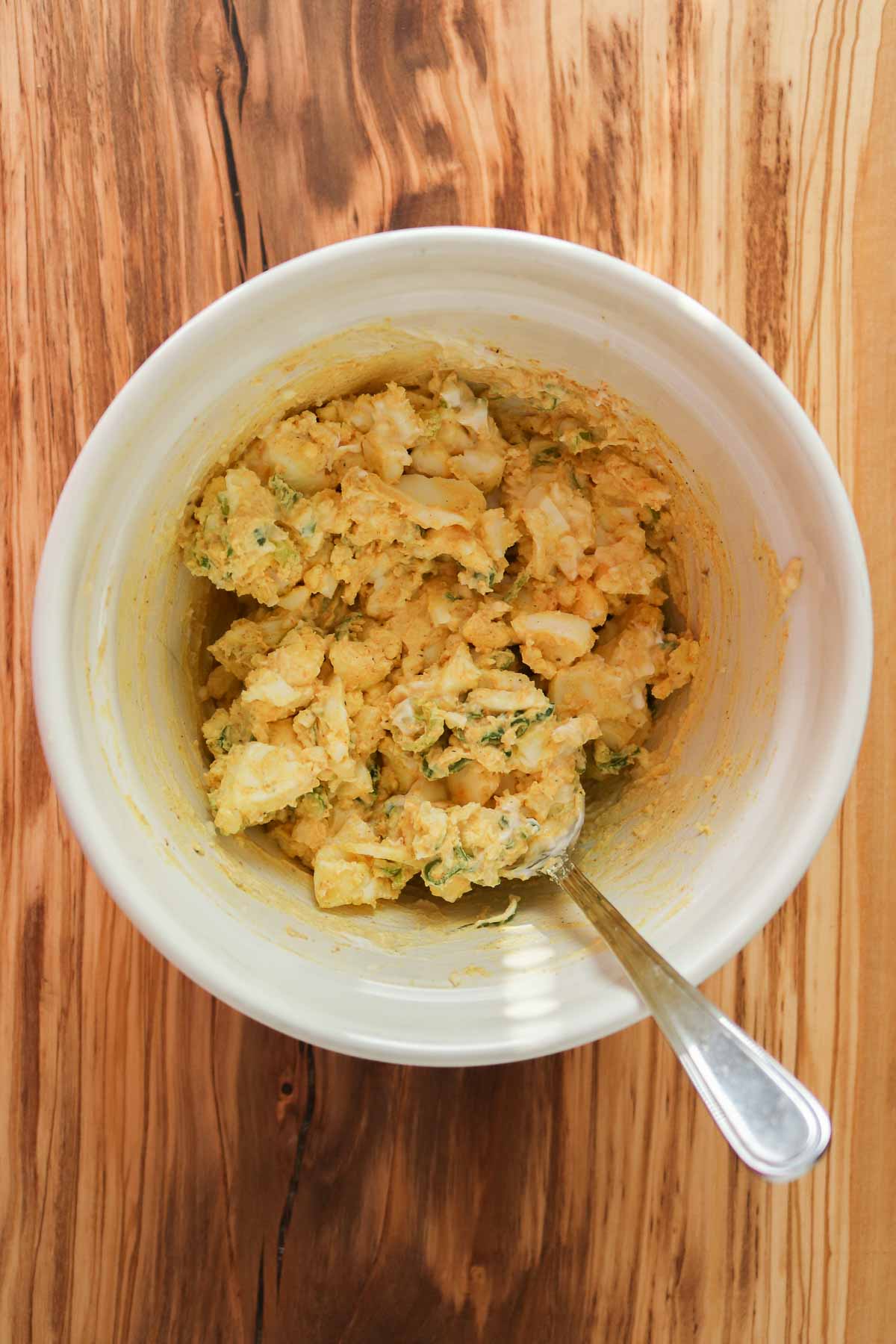 Curry egg salad in a bowl with a spoon.