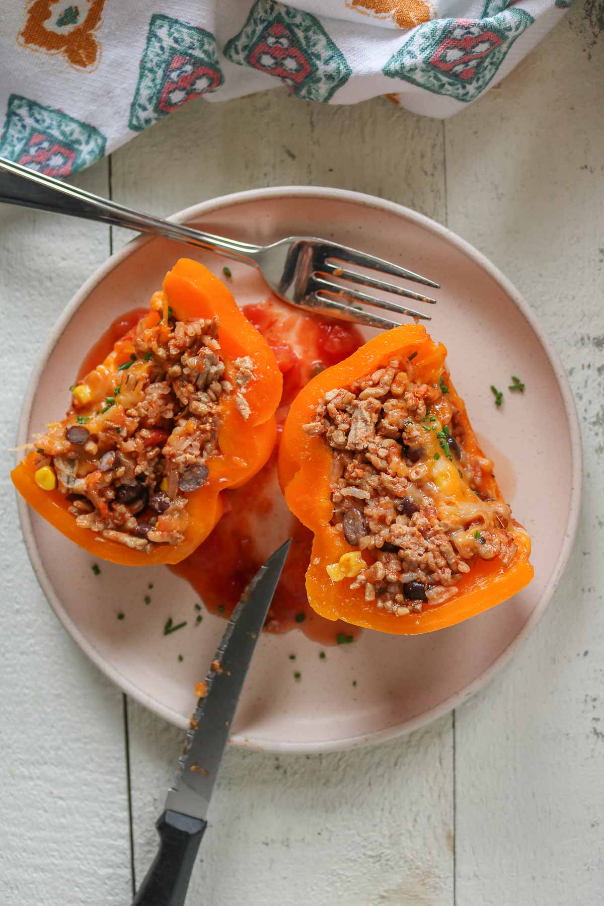 Two halves of a stuffed bell pepper on a plate with a fork and knife.