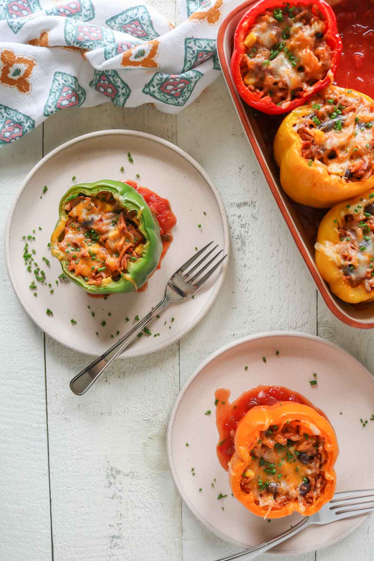 Stuffed bell peppers, three in a baking dish and two others on separate plates with a fork.
