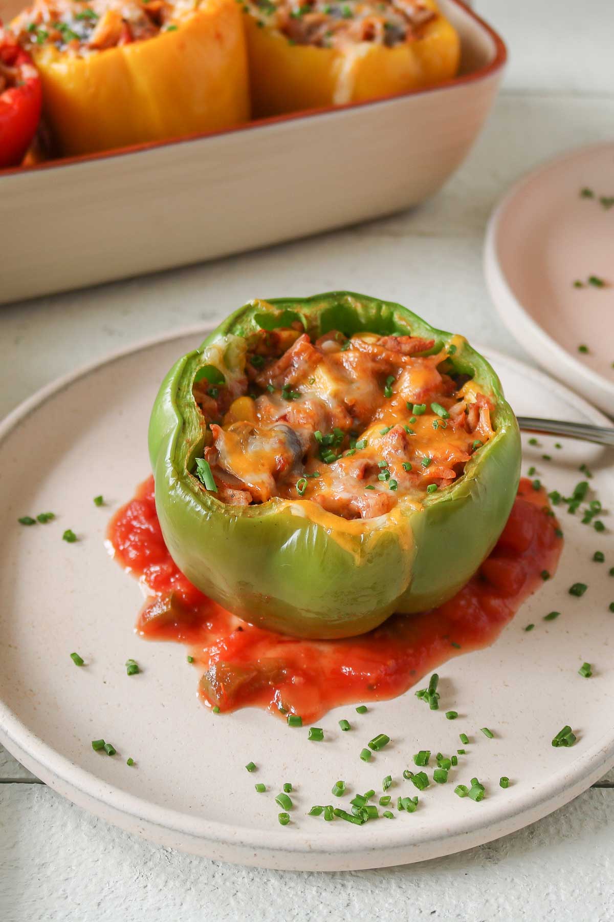 Ground turkey stuffed pepper on a plate with sauce and chives.