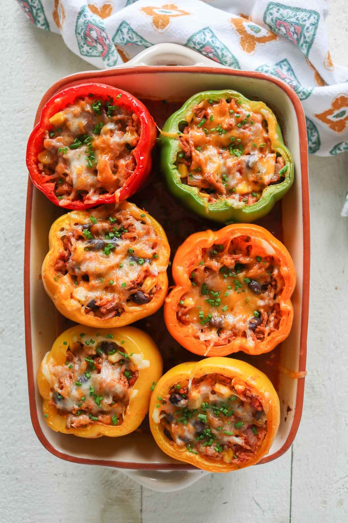 Six baked stuffed peppers in a baking dish garnished with chives.