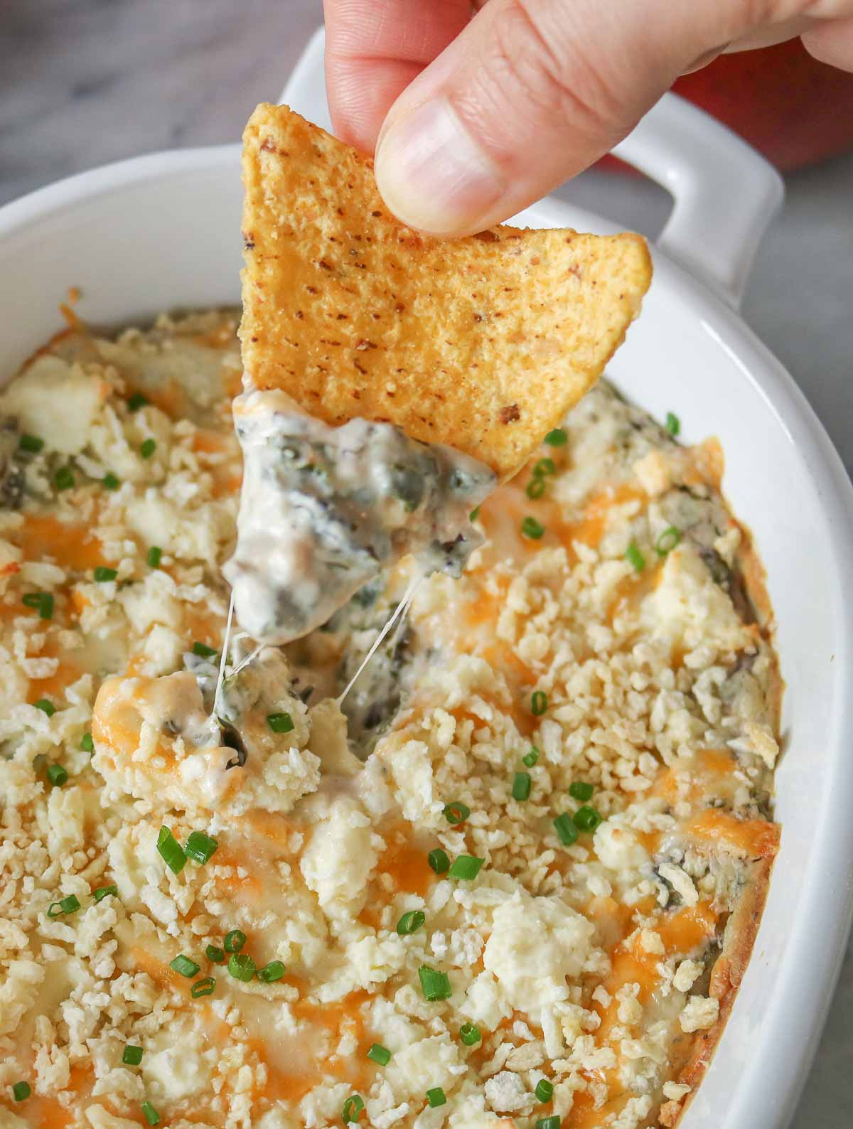 Hand dipping a tortilla chip into cheesy baked kale dip.