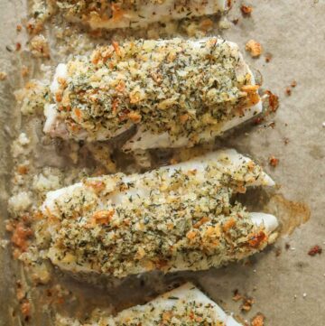 Four baked cod fillets with Newfoundland dressing on a parchment paper-lined sheet pan.