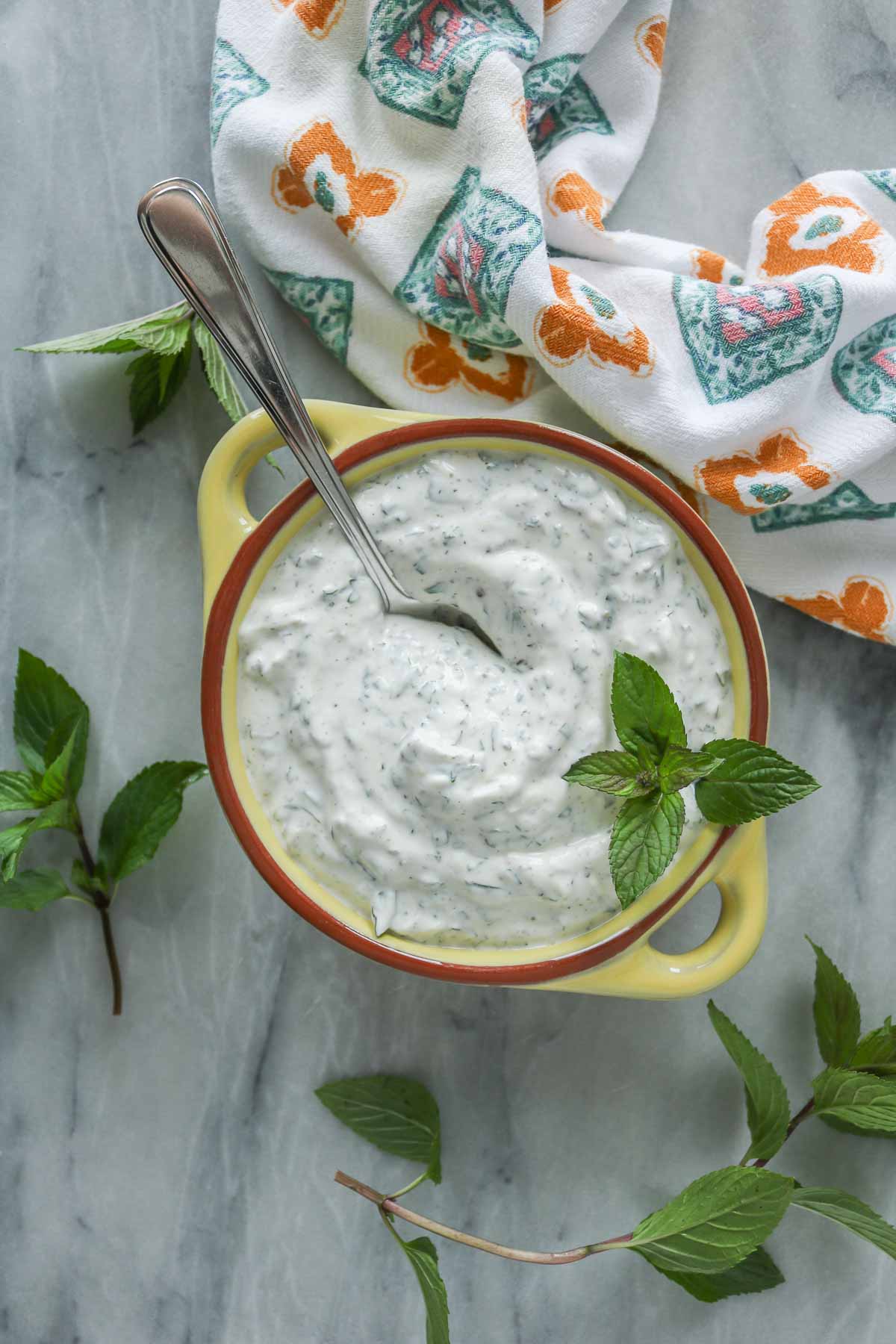 Mint yogurt sauce in a yellow bowl with a spoon.