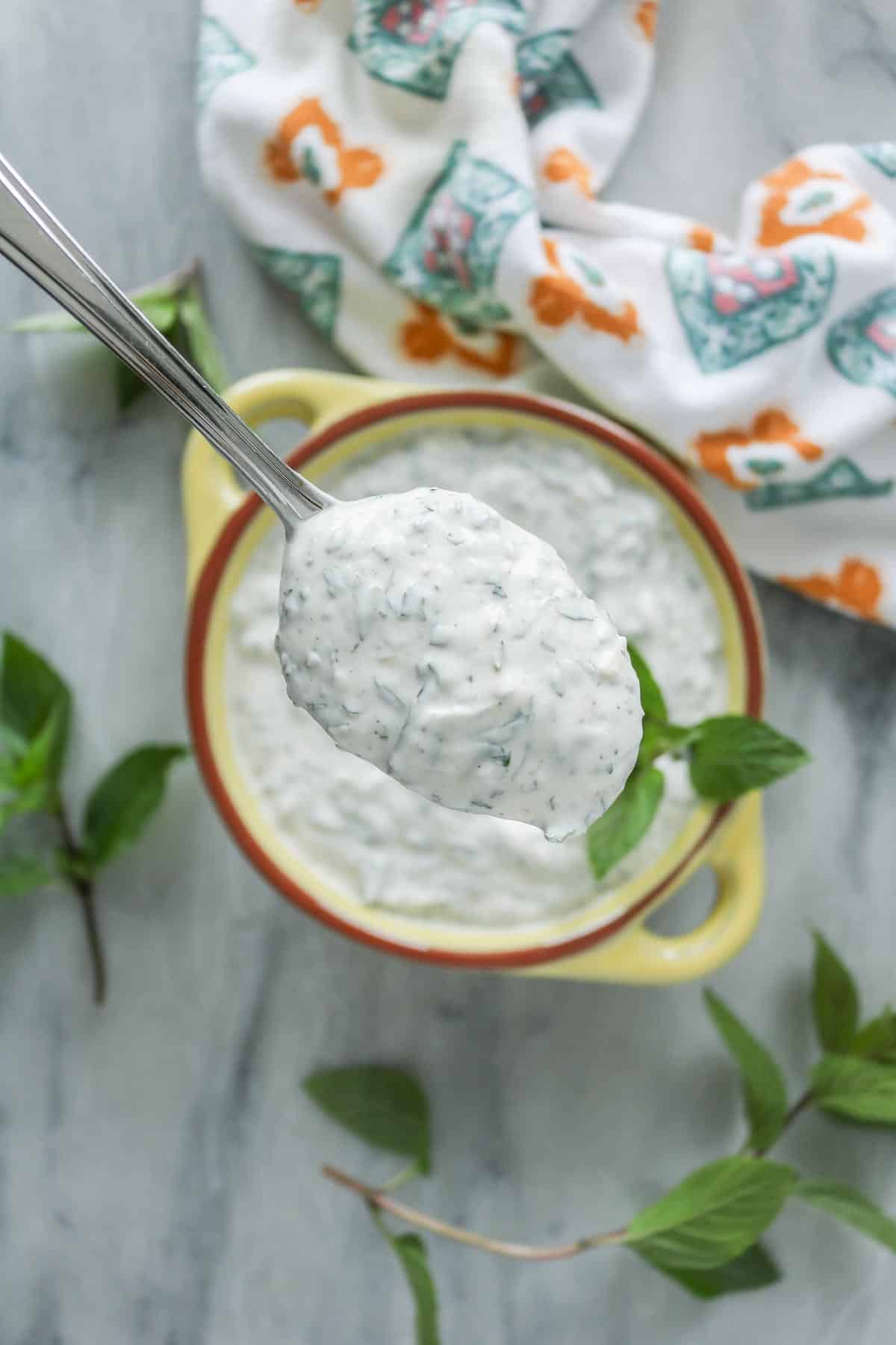Spoonful of mint yogurt sauce from a bowl.