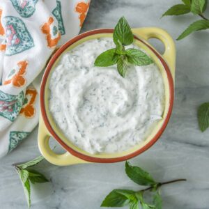 Mint yogurt sauce in a yellow bowl garnished with mint.