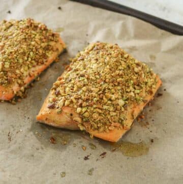 Two baked pistachio-crusted arctic char fillets on a parchment paper-lined sheet pan.