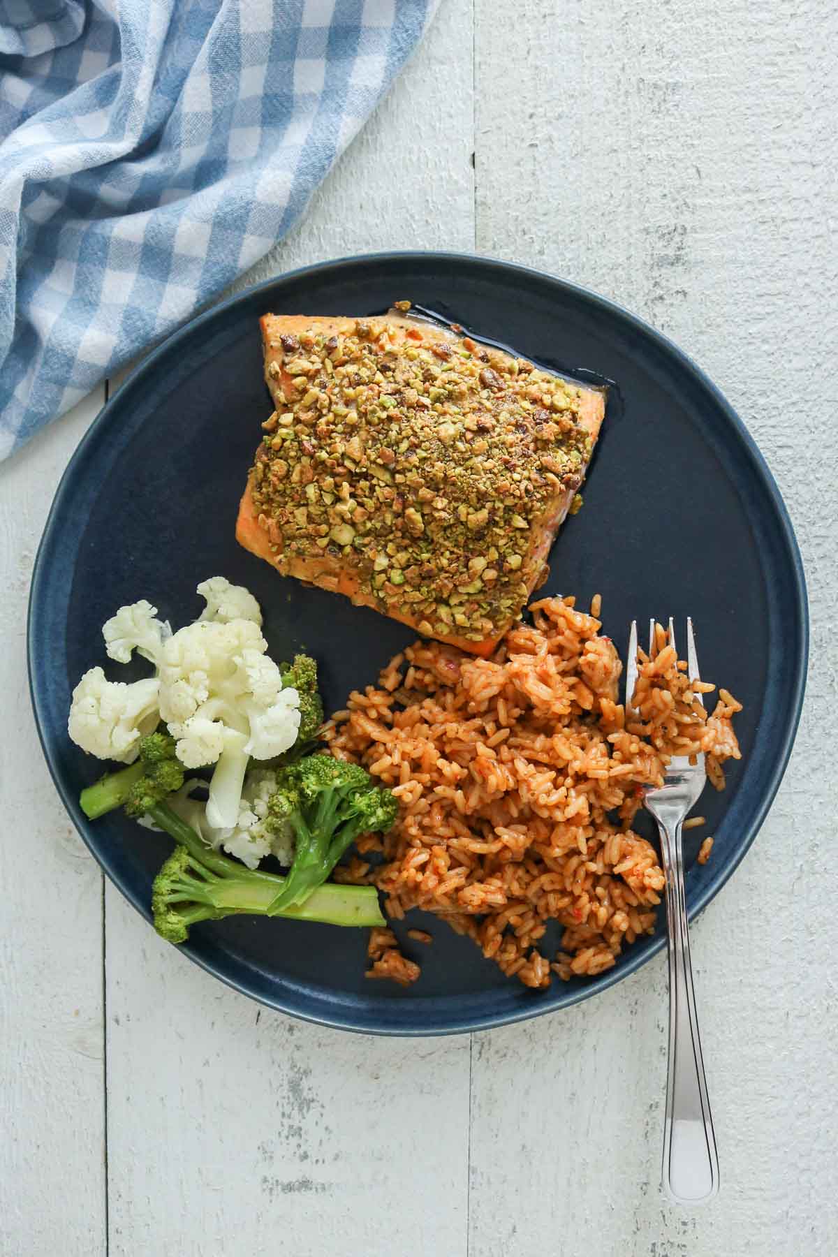 Baked pistachio-crusted arctic char fillet, rice and vegetables on a plate with a fork.