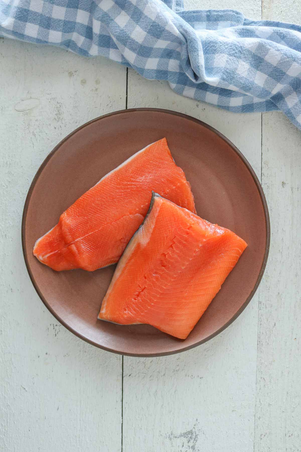 Two uncooked arctic char fillets on a brown plate.