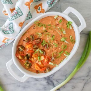 Chili cream cheese dip in a serving dish garnished with green onion and tomatoes.