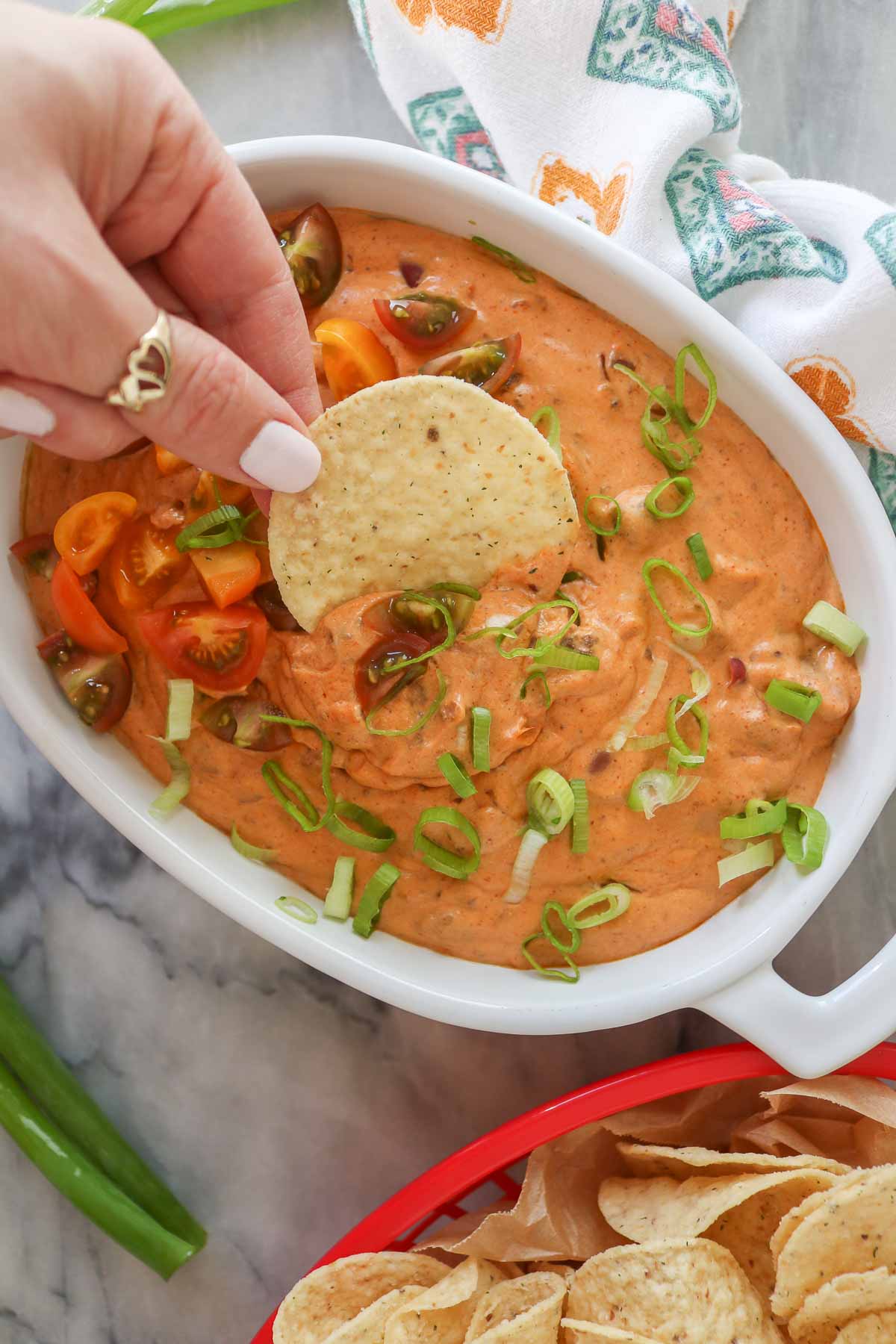 Hand dipping a tortilla chip into a dish of chili cream cheese dip.