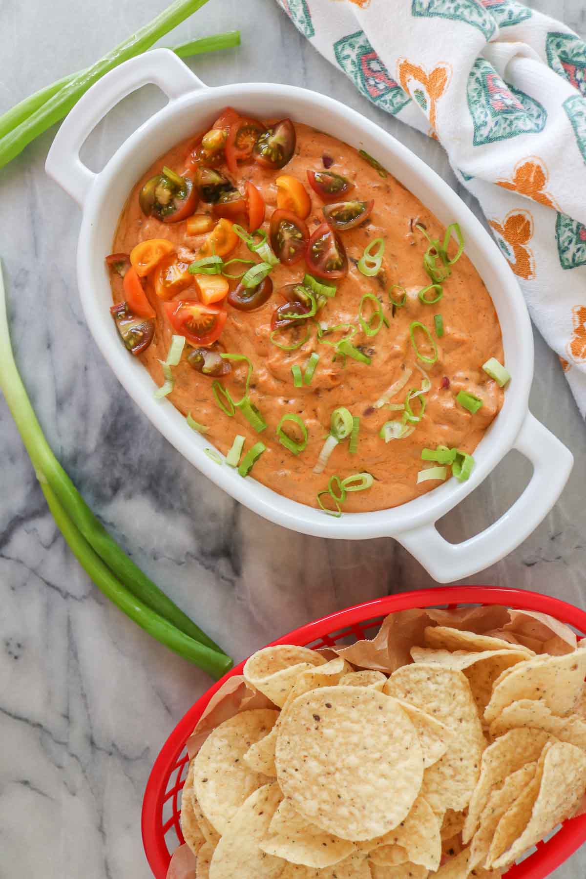 Chili cream cheese dip in a serving dish alongside a basket of tortilla chips.