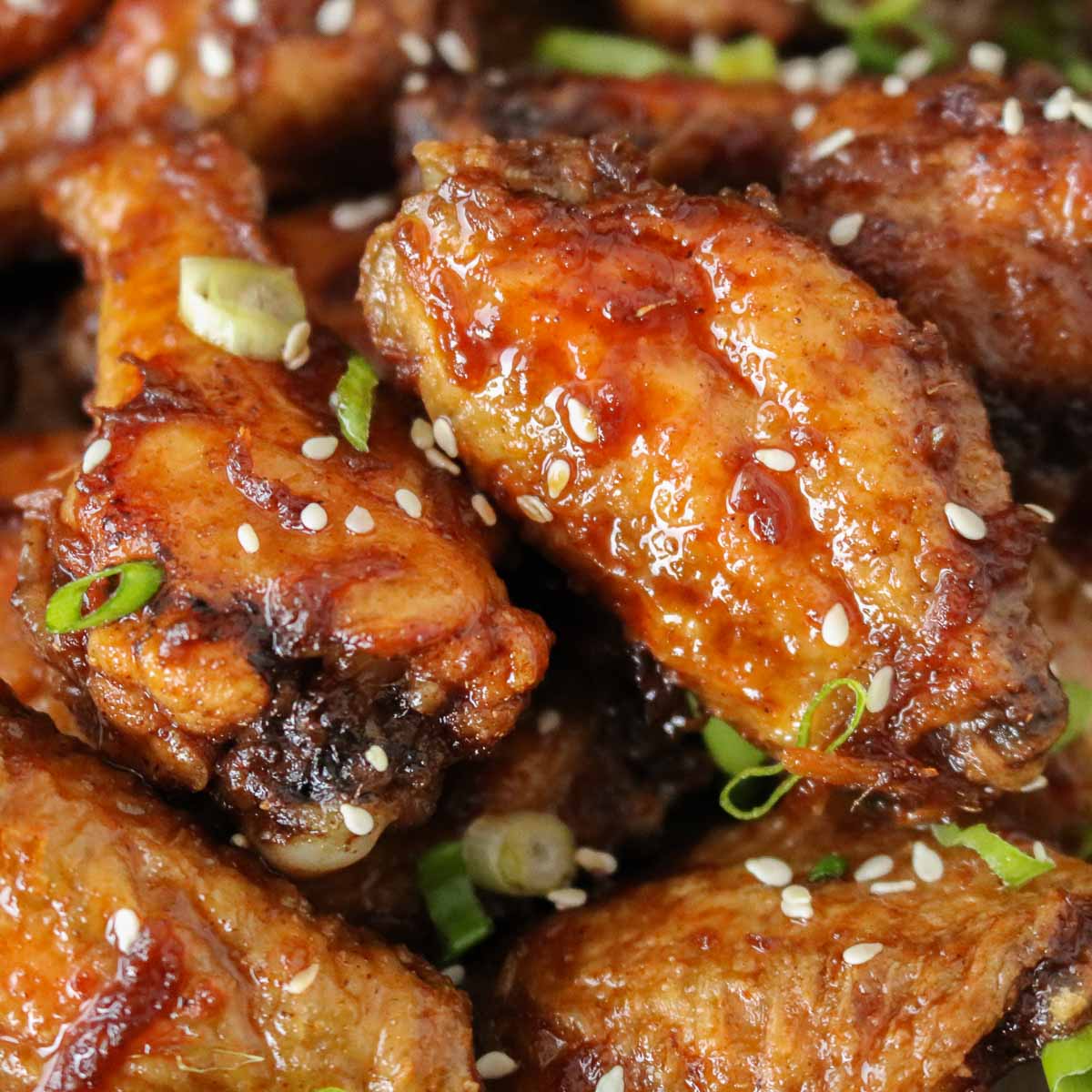 Close-up of crispy soy sauce chicken wings garnished with green onion and sesame seeds.