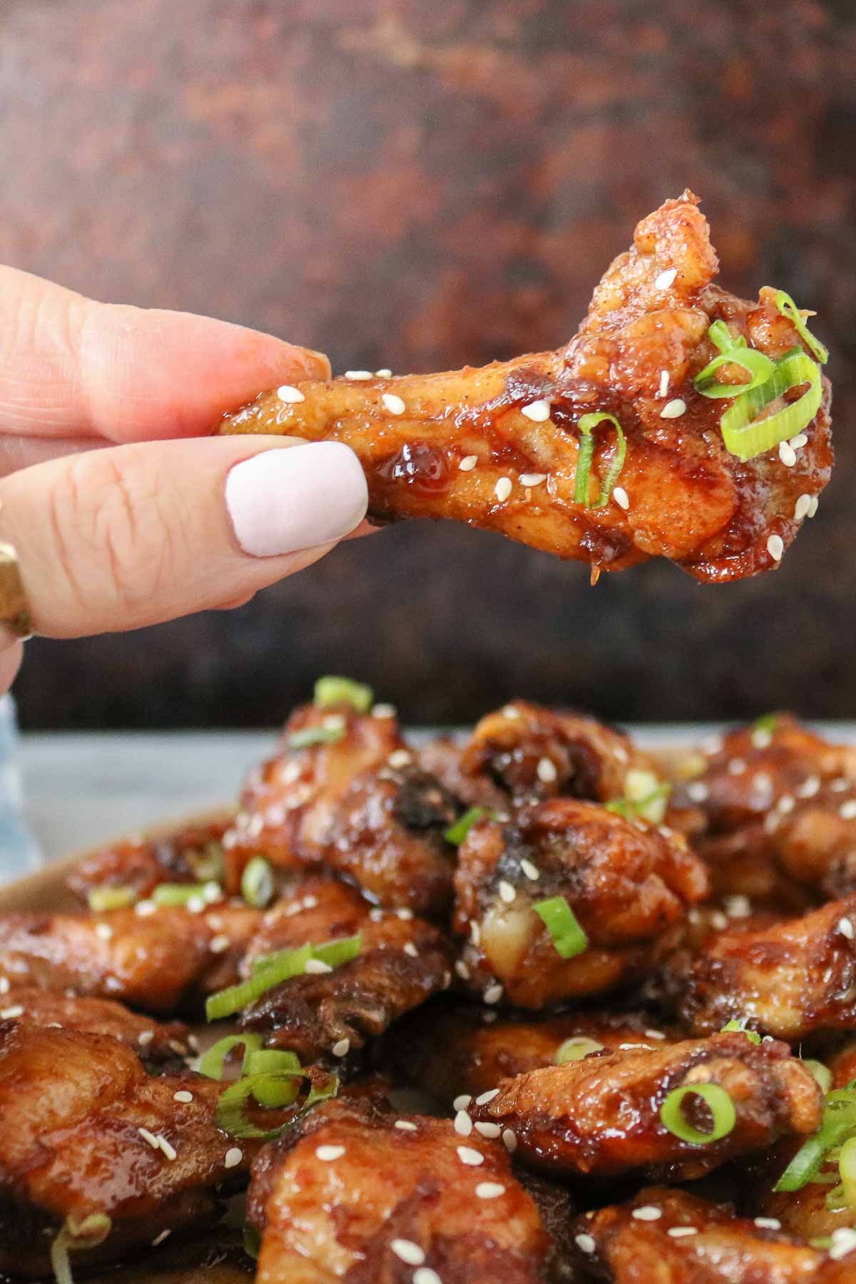 Hand holding a soy sauce chicken wing drumette.