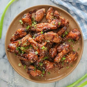 Crispy soy sauce chicken wings on a plate garnished with green onion and sesame seeds.