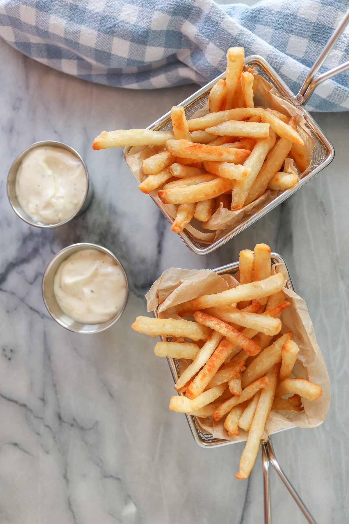 Two servings of fries in stainless steel baskets, each with a serving of truffle mayo.