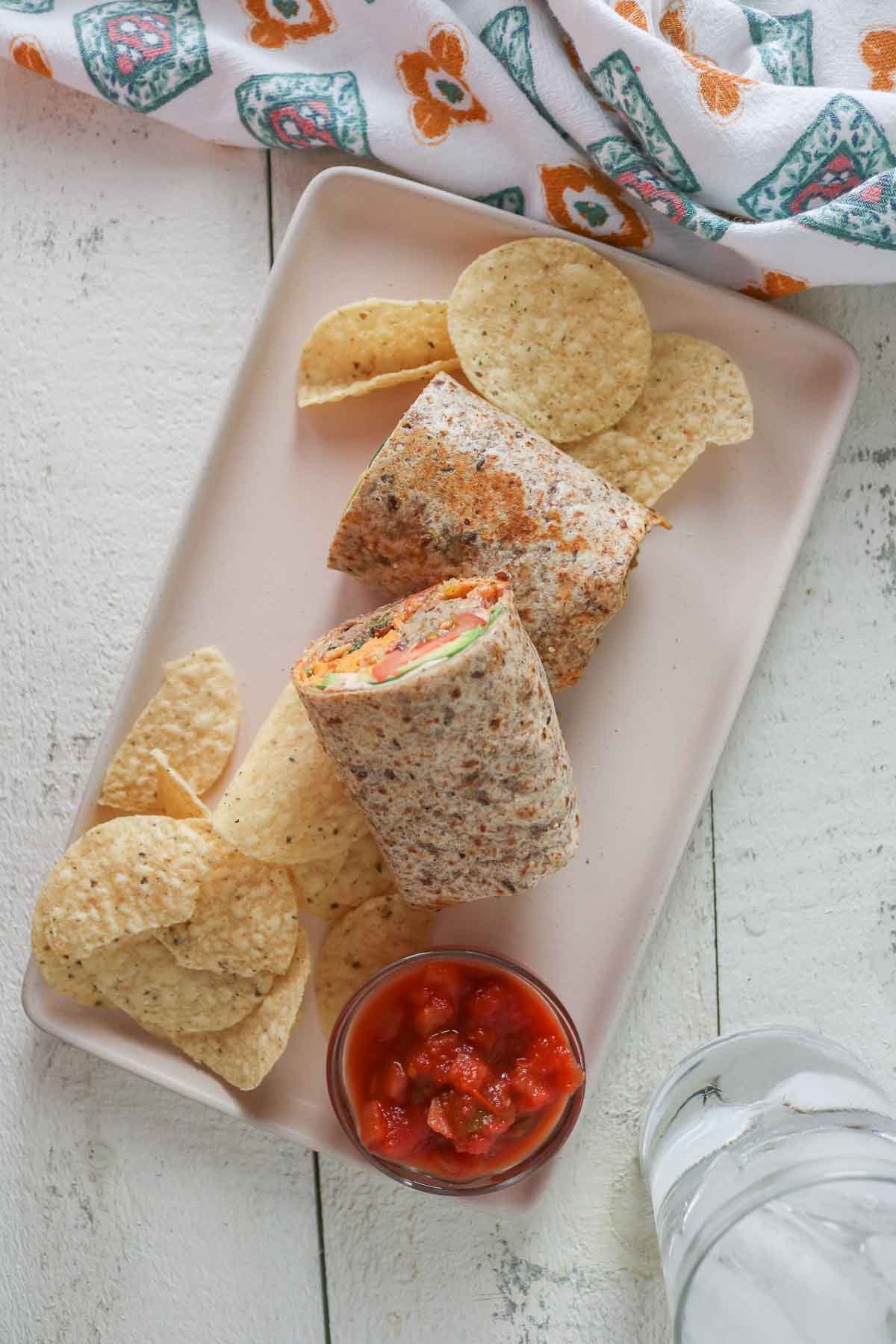Overhead shot of two halves of a meatball wrap, tortilla chips and dish of salsa on a plate.