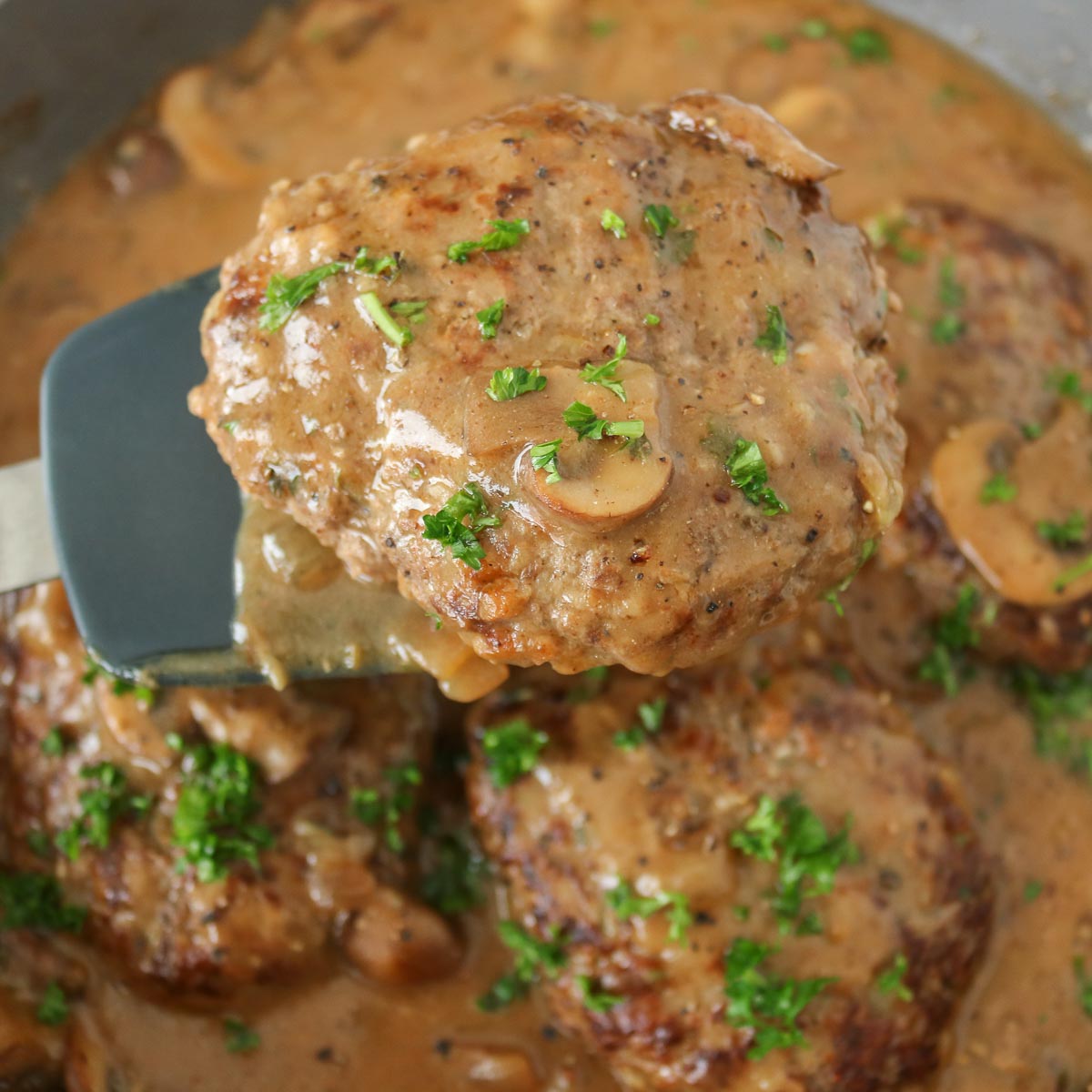 Spatula serving a portion of Salisbury steak from a frying pan.