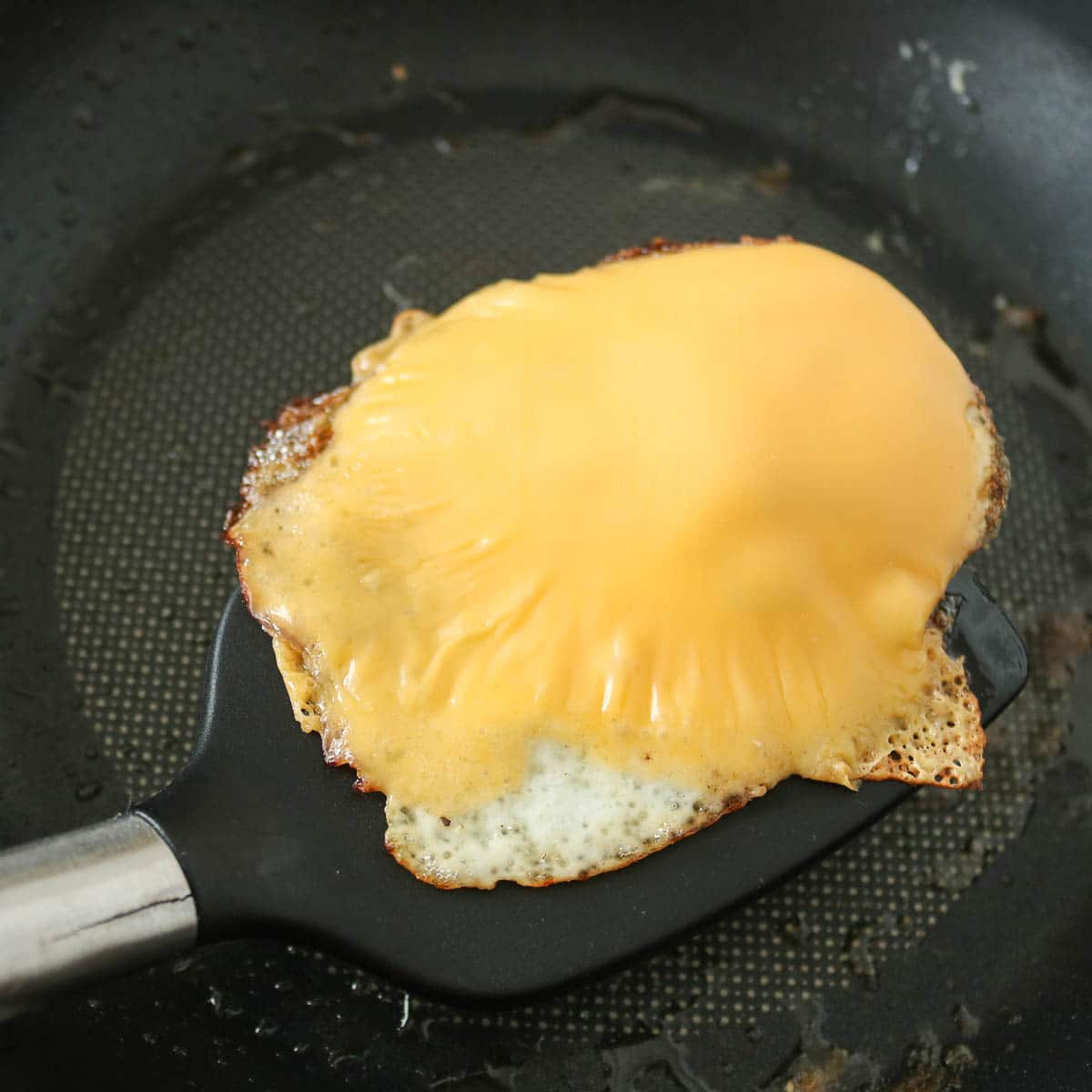 Spatula serving a cheesy fried egg from a frying pan.