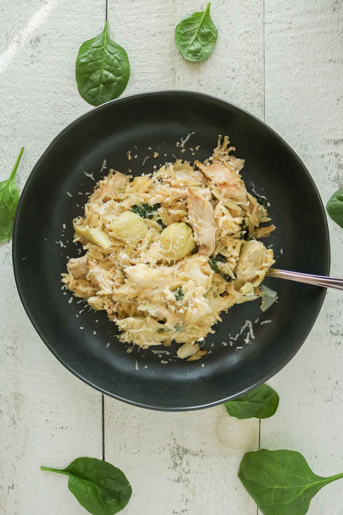 Portion of orzo bake in a black bowl with a fork.