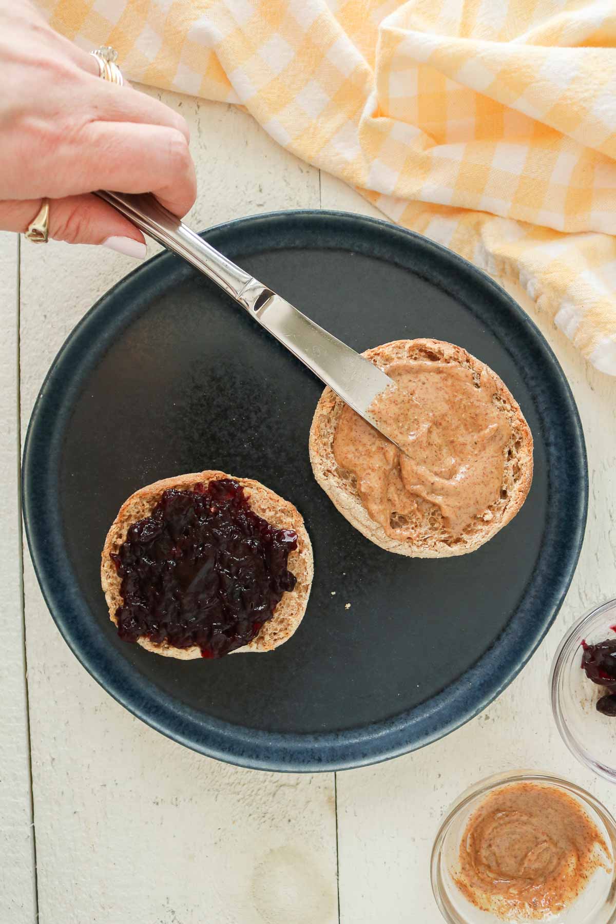 Spreading almond butter and jam over an English muffin.