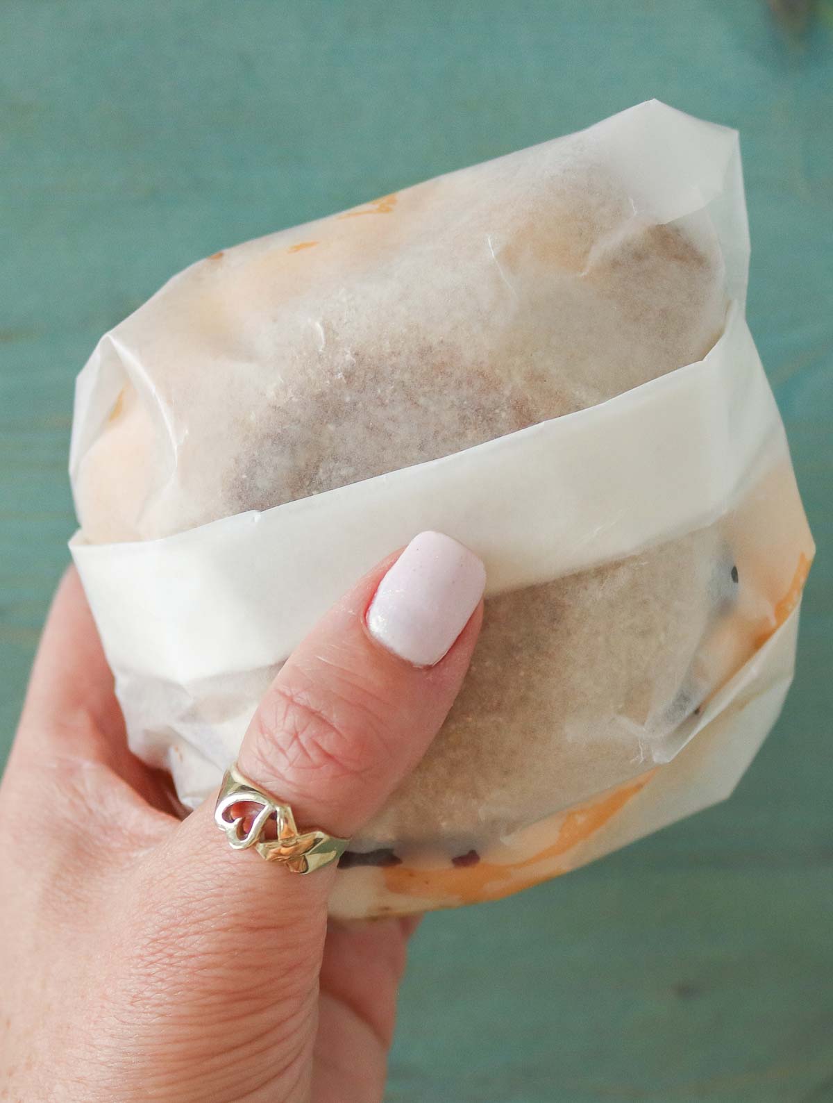 Hand holding a wax paper-wrapped breakfast sandwich.