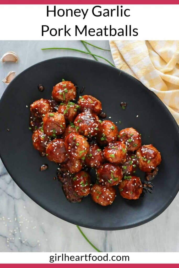 Honey garlic pork meatballs on a serving platter garnished with chives and sesame seeds.