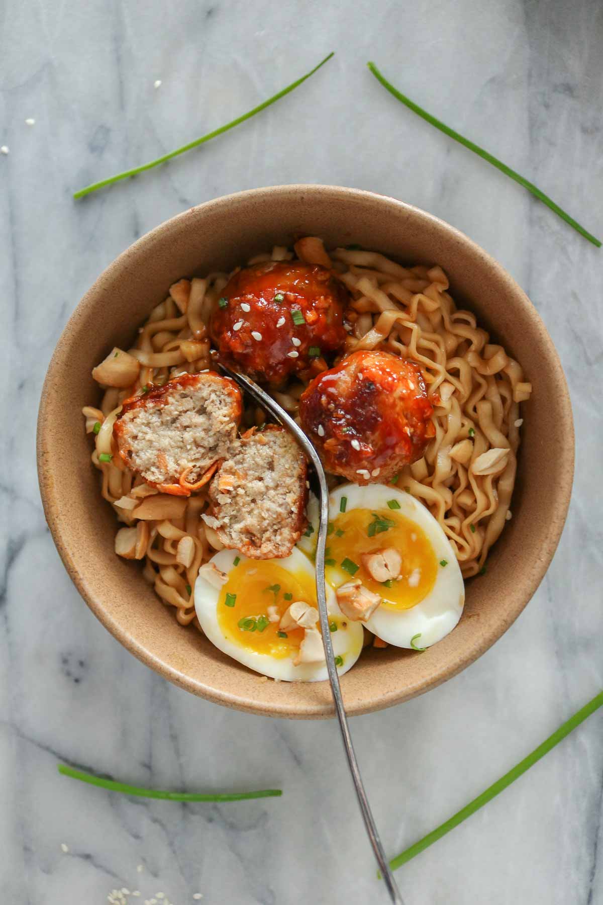 Meatballs, noodles and a jammy soft-boiled egg in a bowl with one of the meatballs cut in half.