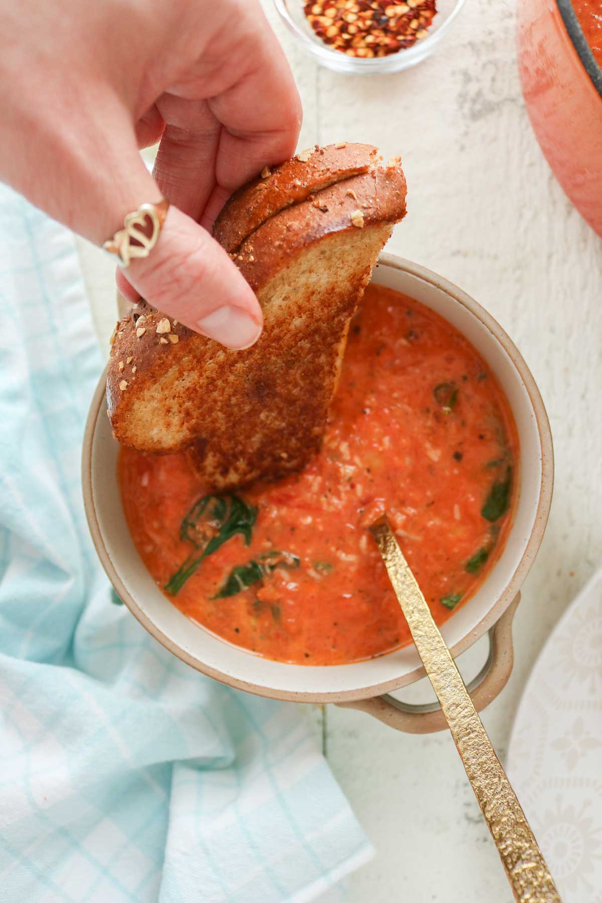 Hand dipping half of a grilled cheese sandwich into a bowl of soup.
