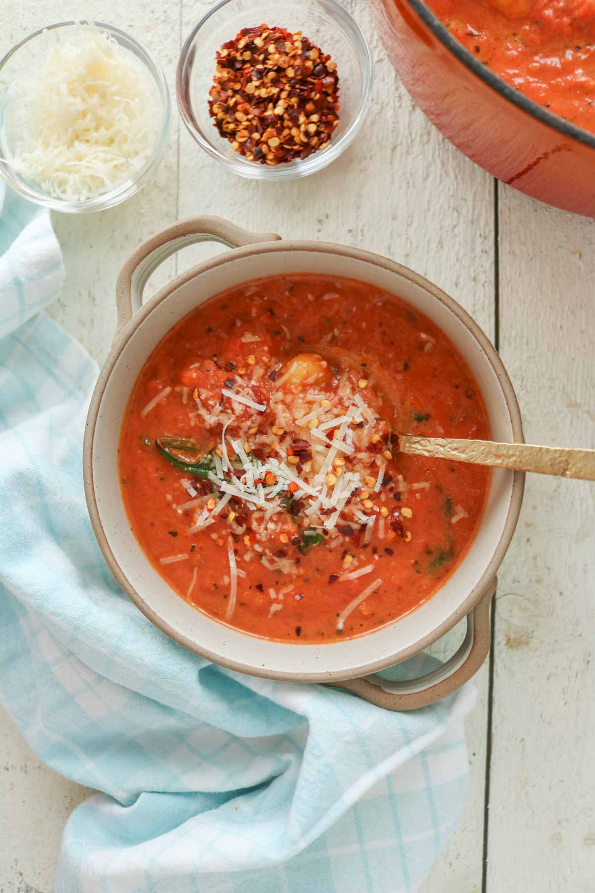 Bowl of creamy tomato gnocchi soup with Parmesan cheese and crushed red pepper flakes.