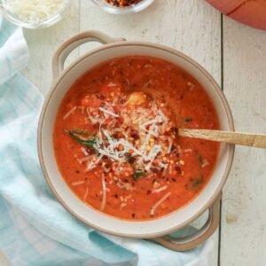 Bowl of creamy tomato gnocchi soup with Parmesan cheese and crushed red pepper flakes.