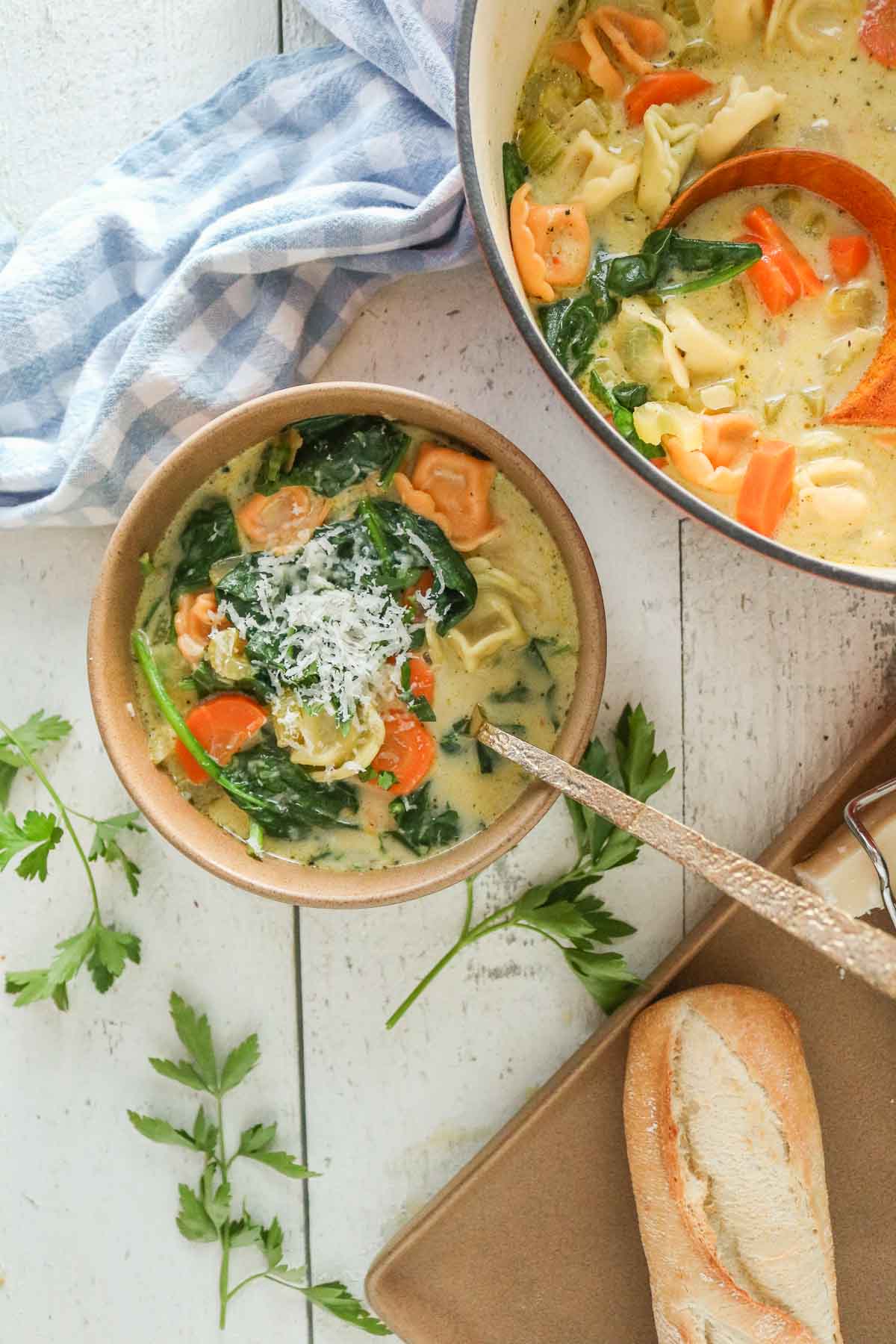 Creamy tortellini soup in a bowl next to a pot of soup and baguette.