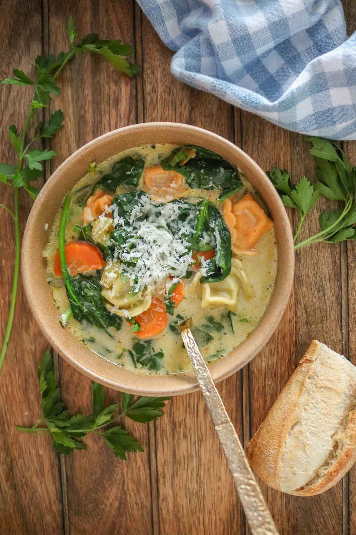 Bowl of creamy vegetable tortellini soup next to a piece of baguette.