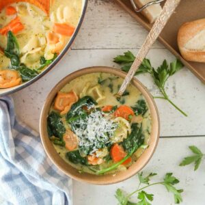 Creamy tortellini soup in a bowl next to a pot of soup and baguette.