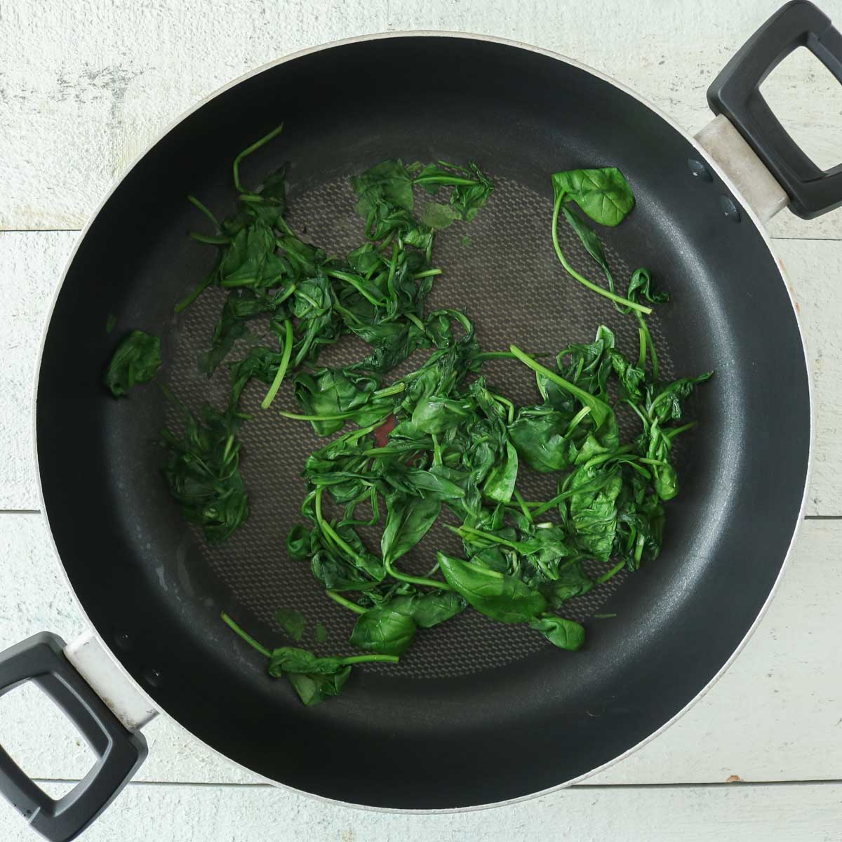Cooked baby spinach in a frying pan.