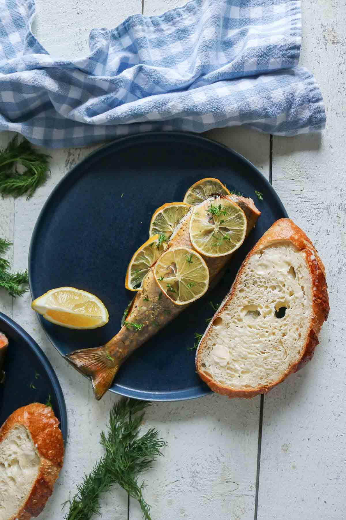 Baked trout with a slice of bread and lemon wedge on a plate.