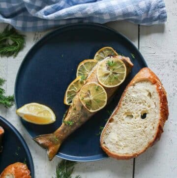 Baked trout with a slice of bread and lemon wedge on a plate.