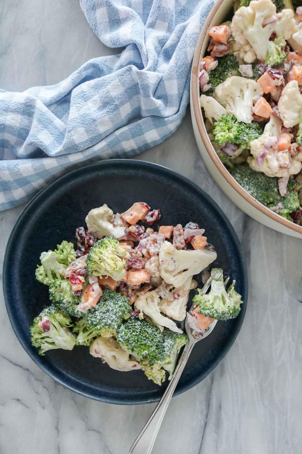 Cauliflower broccoli salad: some in a serving dish and some on a plate with a fork.