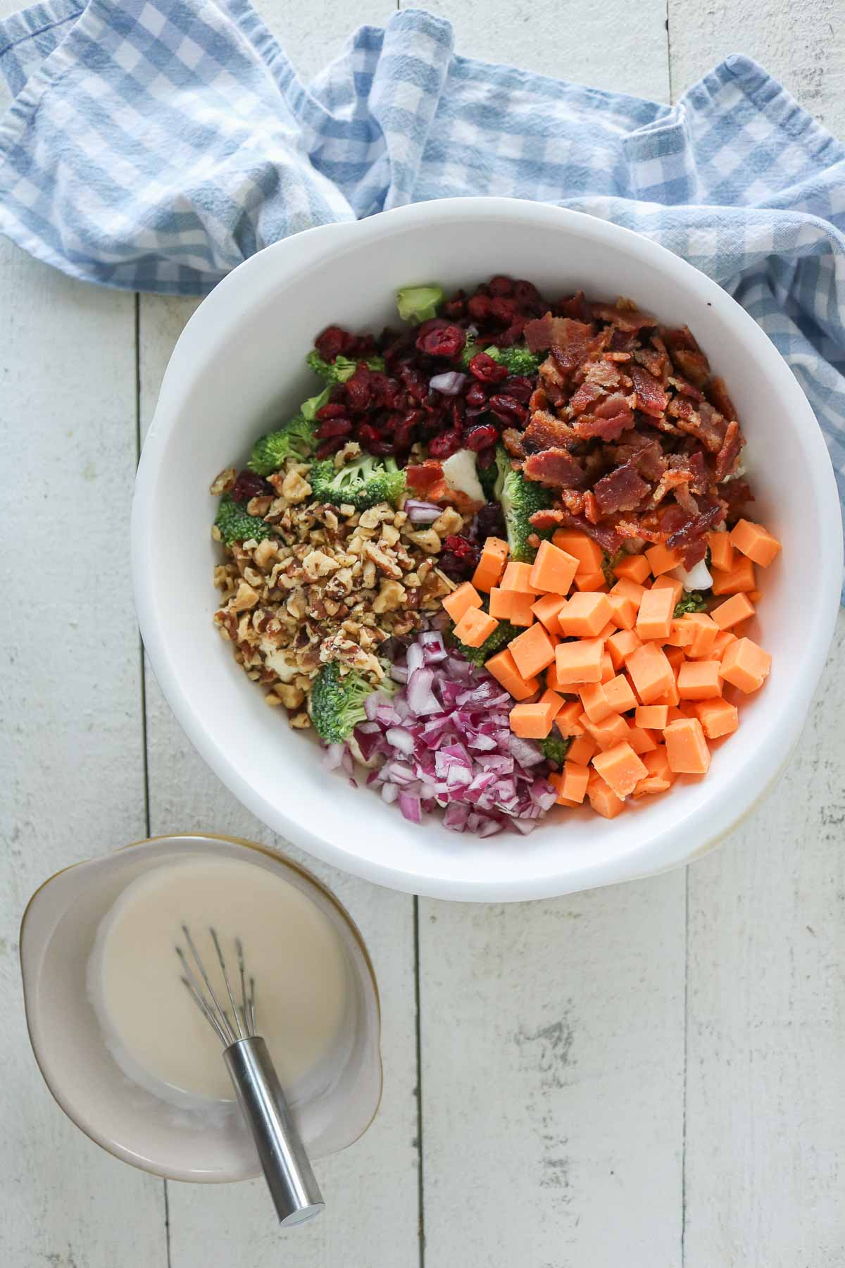 Cauliflower broccoli salad ingredients in a bowl alongside a bowl of dressing.